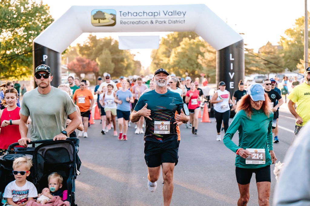 A group of people running and walking in a marathon event under a Tehachapi Valley Recreation & Park District arch.