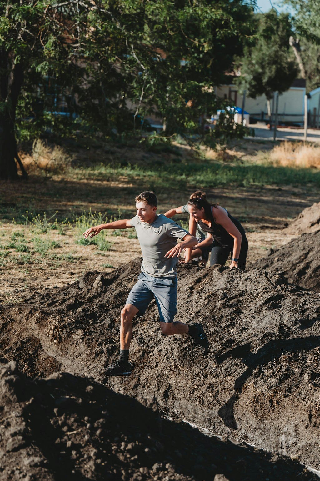 Two people running on uneven, muddy terrain in an outdoor obstacle course.