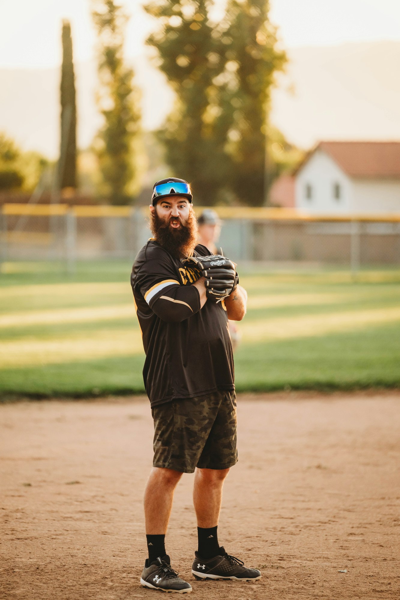 Bearded man with sunglasses and baseball glove on a sunny field.