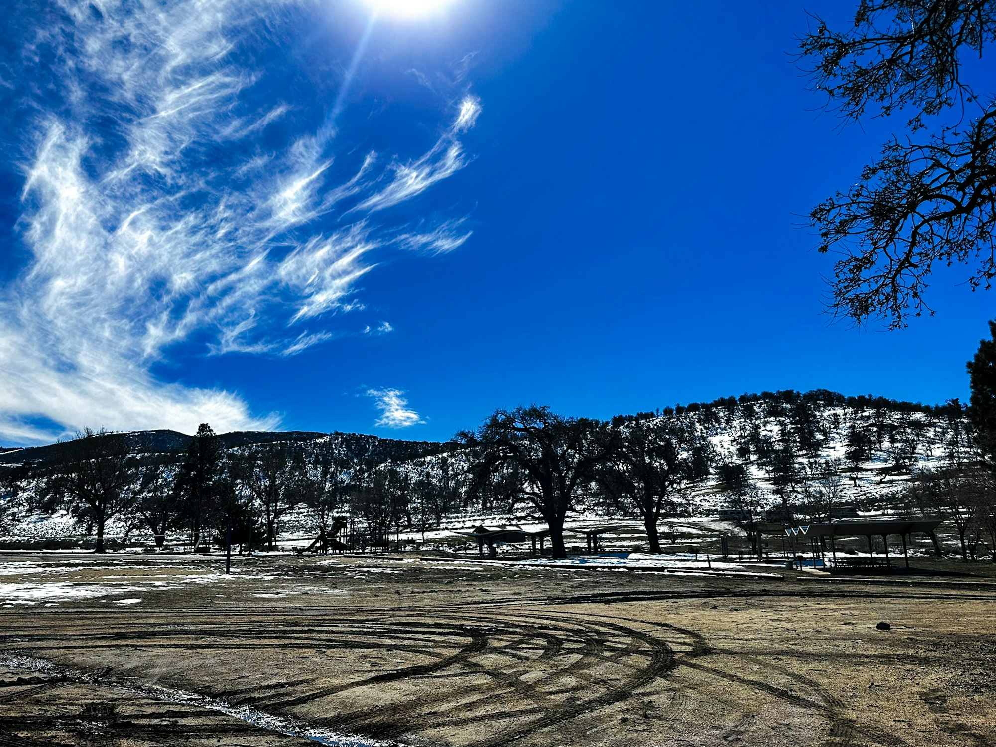 A blue sky with wispy clouds over a snowy landscape with trees and tire tracks.