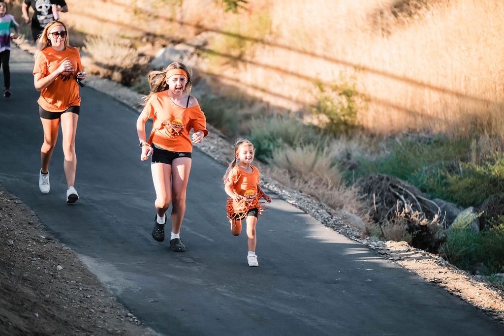 People running on a paved path outdoors, wearing orange shirts.