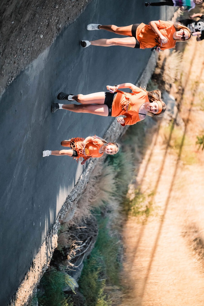 People running on a paved path outdoors, wearing orange shirts.