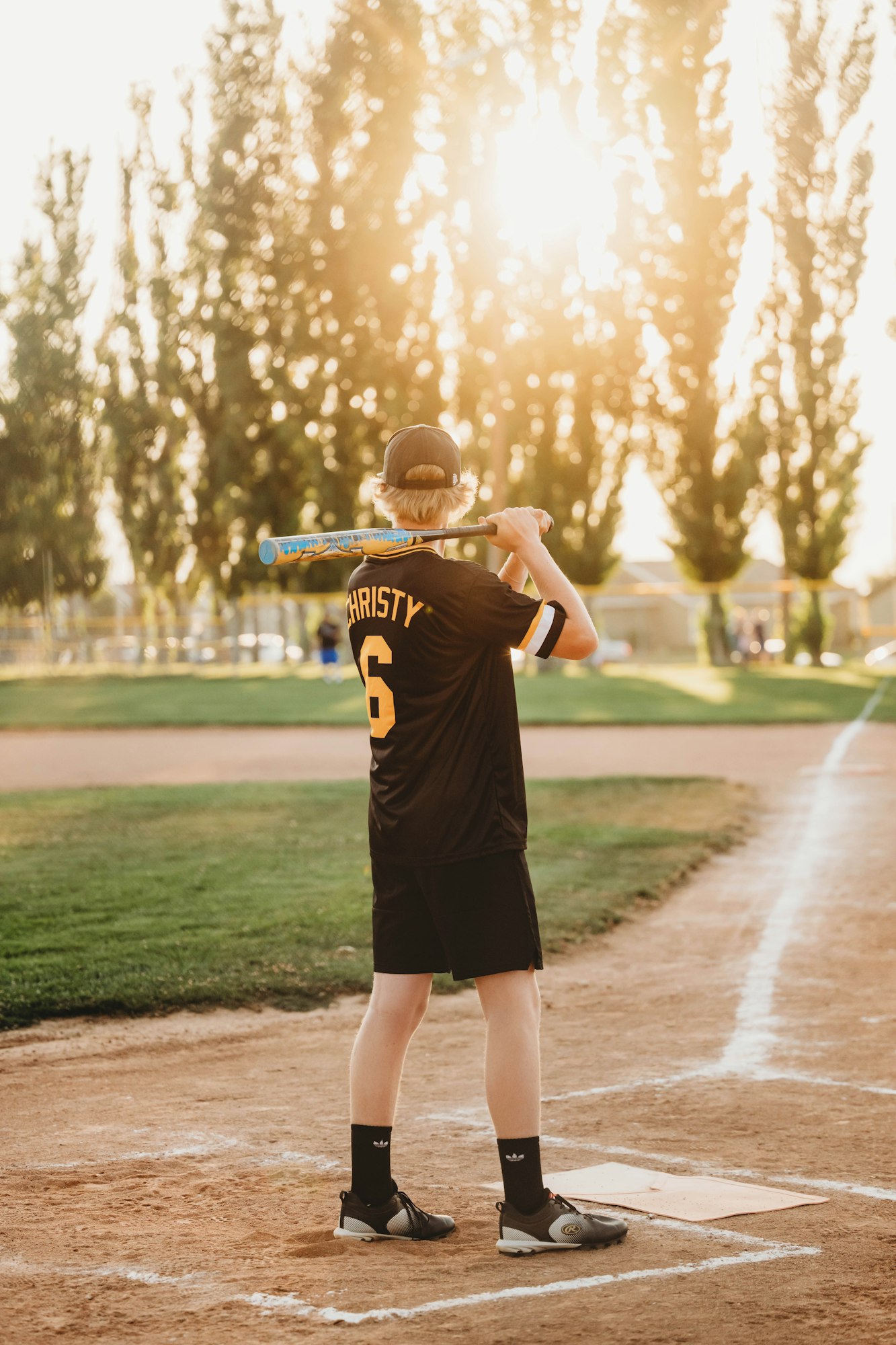 A person playing baseball, standing at home plate with a bat on their shoulder, during a sunny day.