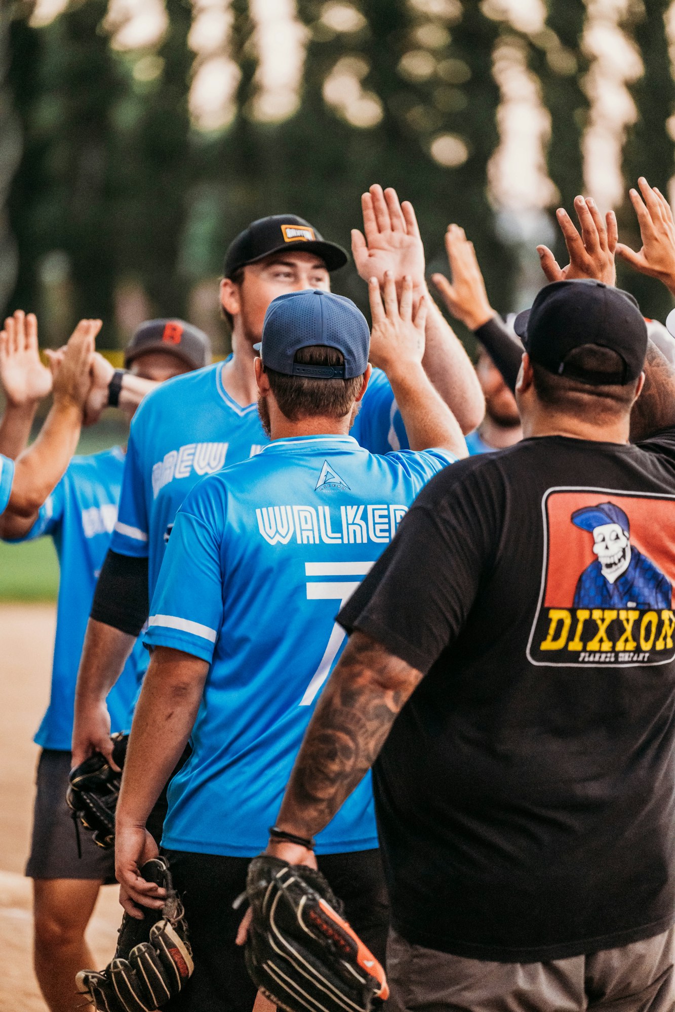 A softball team in blue and black jerseys high-fiving after a game.