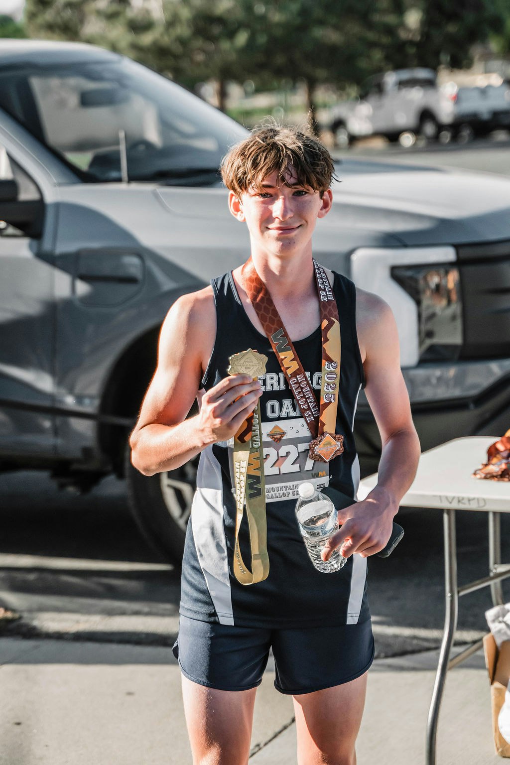 Runner holding medals and a water bottle, wearing a bib labeled "322".