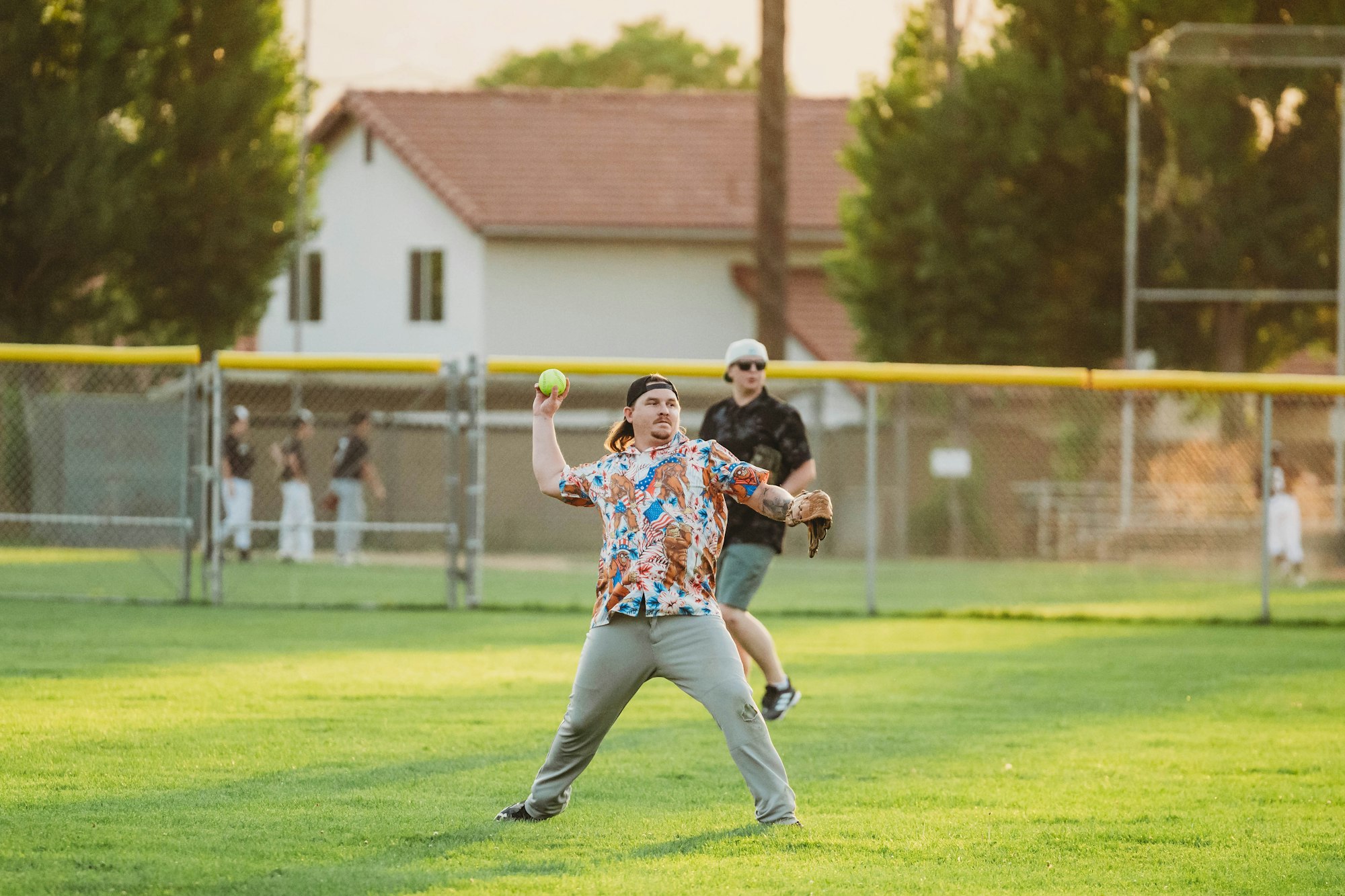 A person in a colorful shirt throws a ball while another person watches in a grassy field during what appears to be a game.