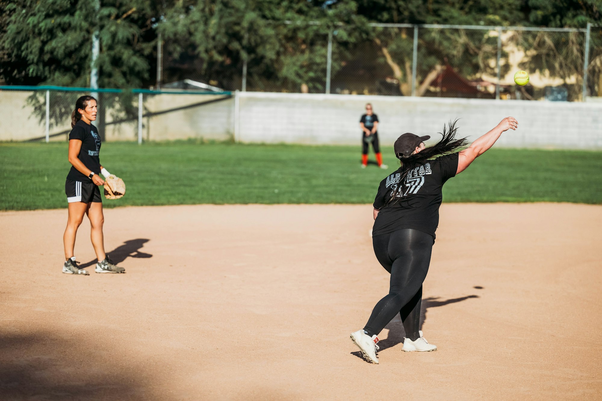 Women playing softball, one pitching and others ready to field.