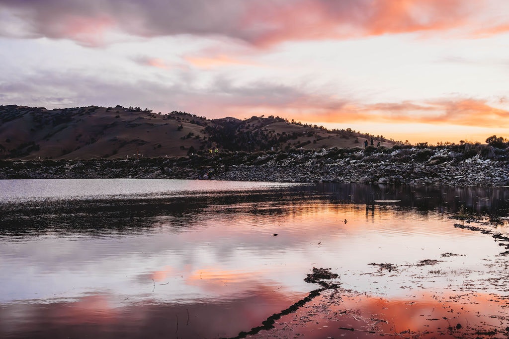 A serene lake at sunset with reflections of hills and colorful sky.