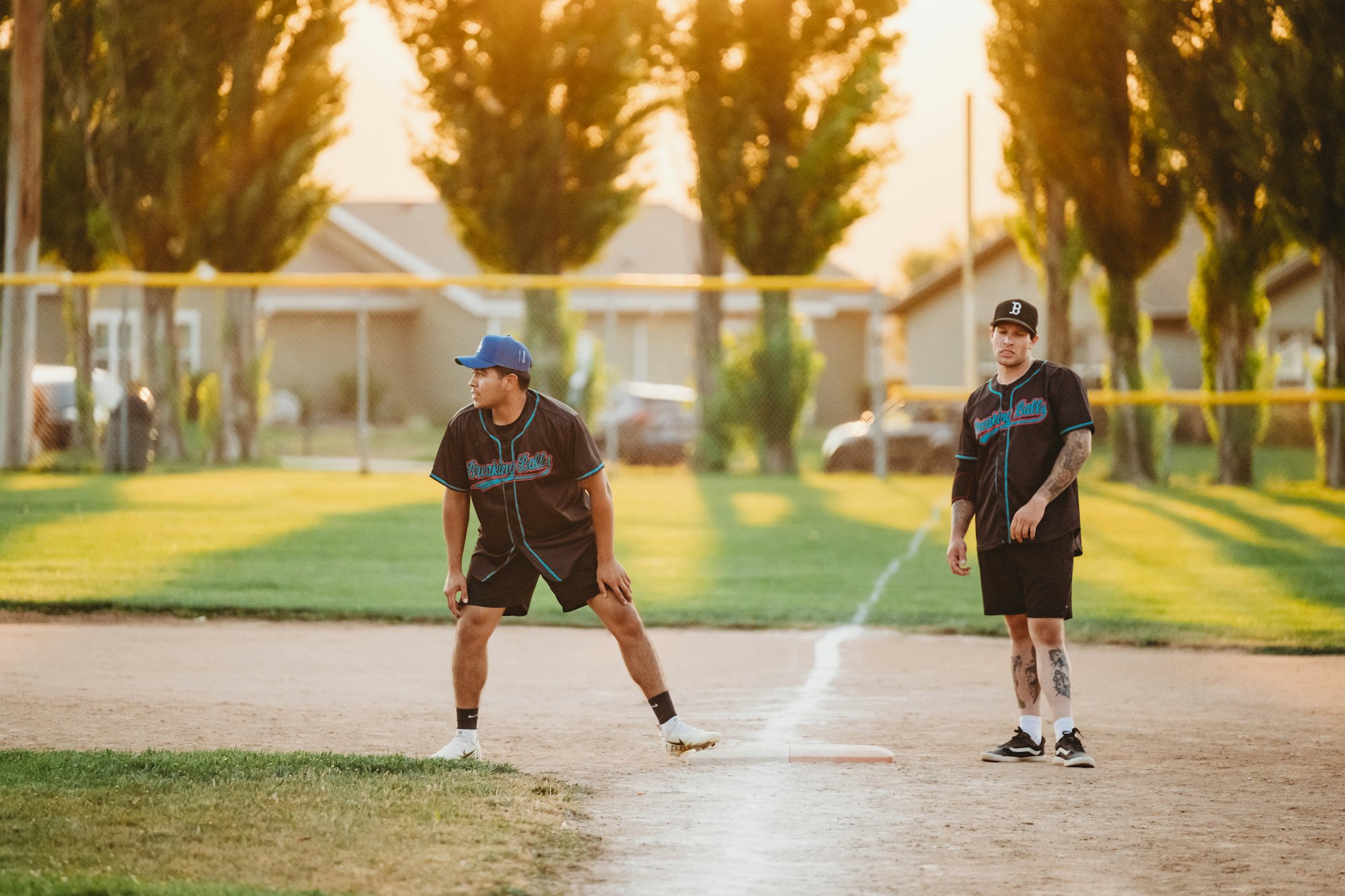 Two people on a baseball field at sunset, wearing team uniforms and caps, with a focus on sports and teamwork.
