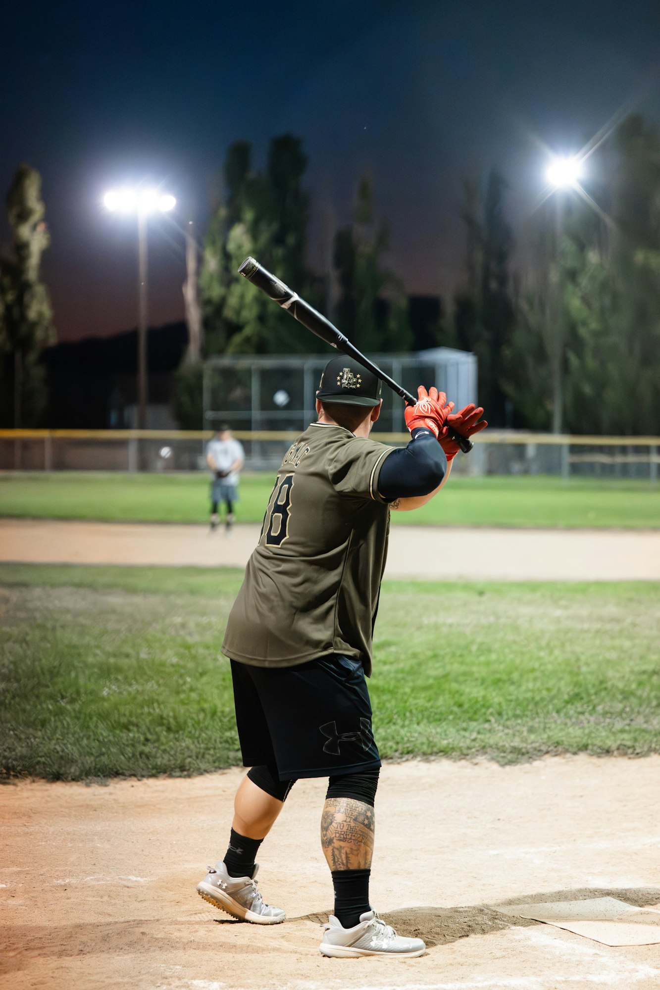 A batter prepares to swing at a night-time baseball game under bright lights.
