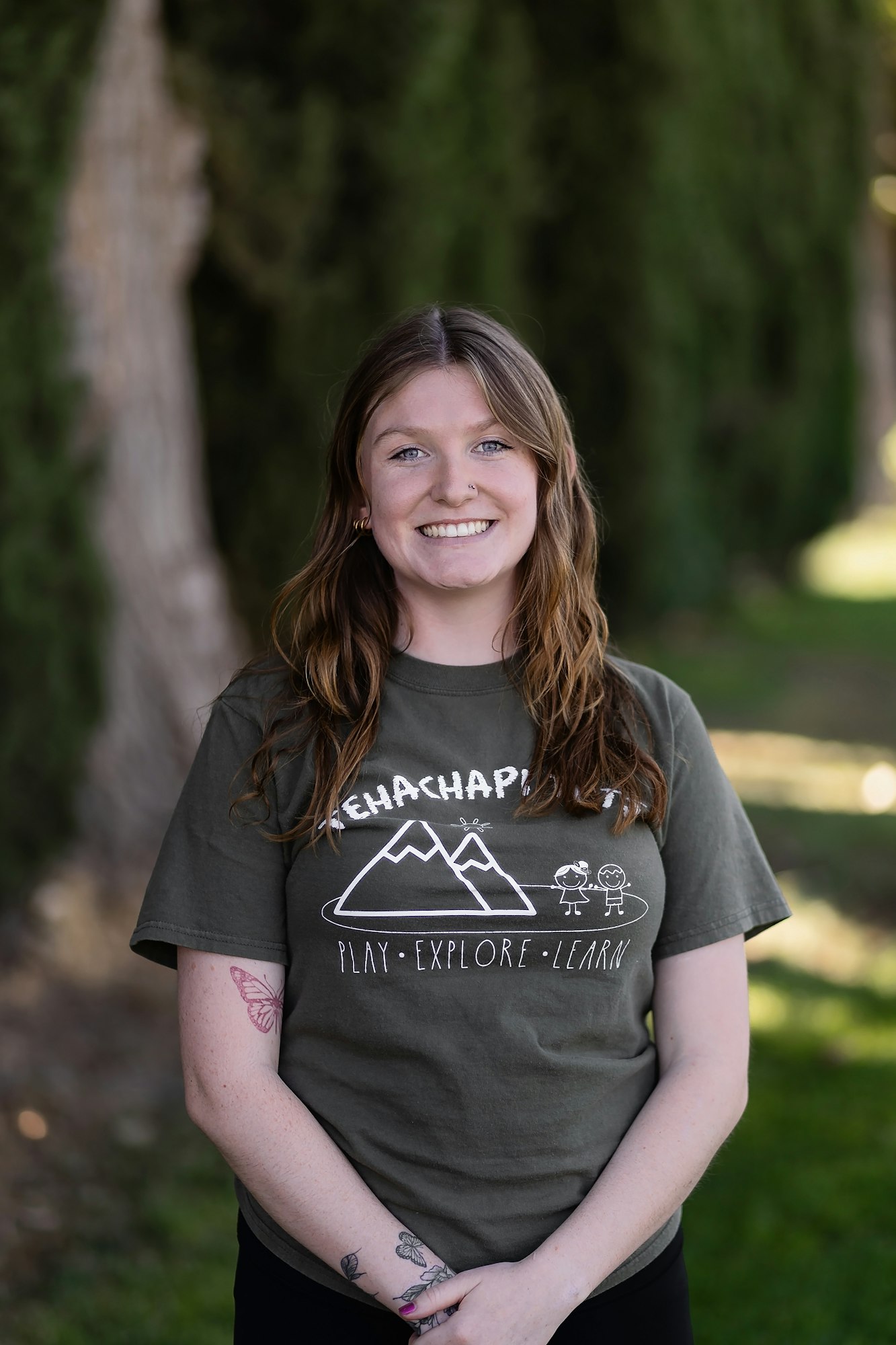 A person wearing a "Tehachapi" shirt with a mountain and children design, standing outdoors with trees in the background.