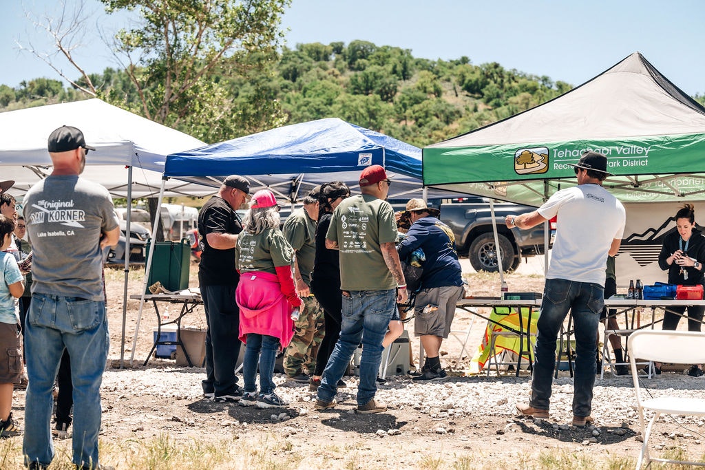 An outdoor event with people gathered under tents, possibly a community fair or local gathering.