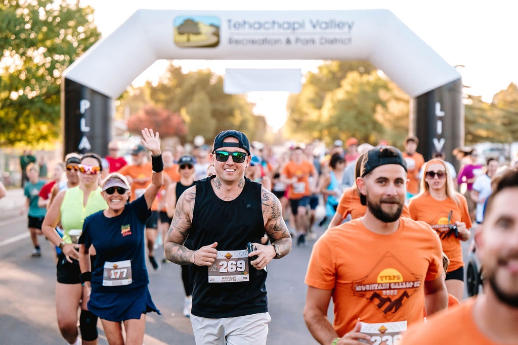 Runners participating in an outdoor race beneath an inflatable start archway, with some smiling and waving.