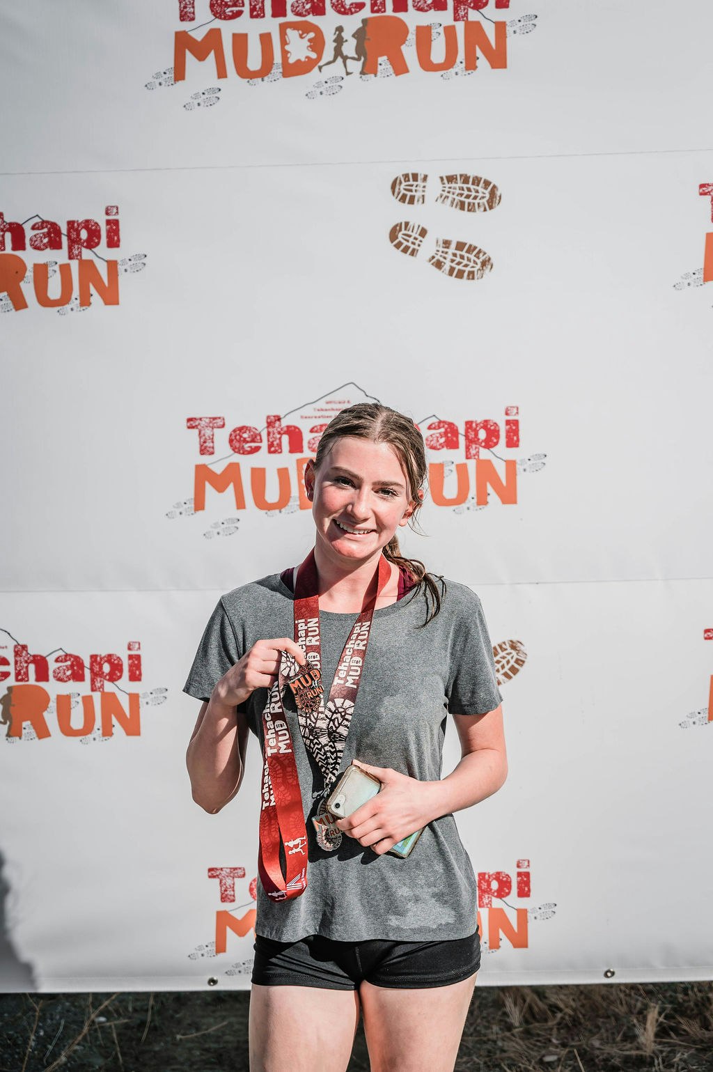 A person holding medals stands against a backdrop with "Tehachapi Mud Run" branding.