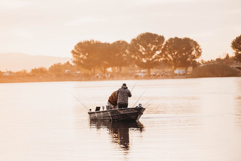 A person fishing from a boat on a calm lake during a golden sunset.