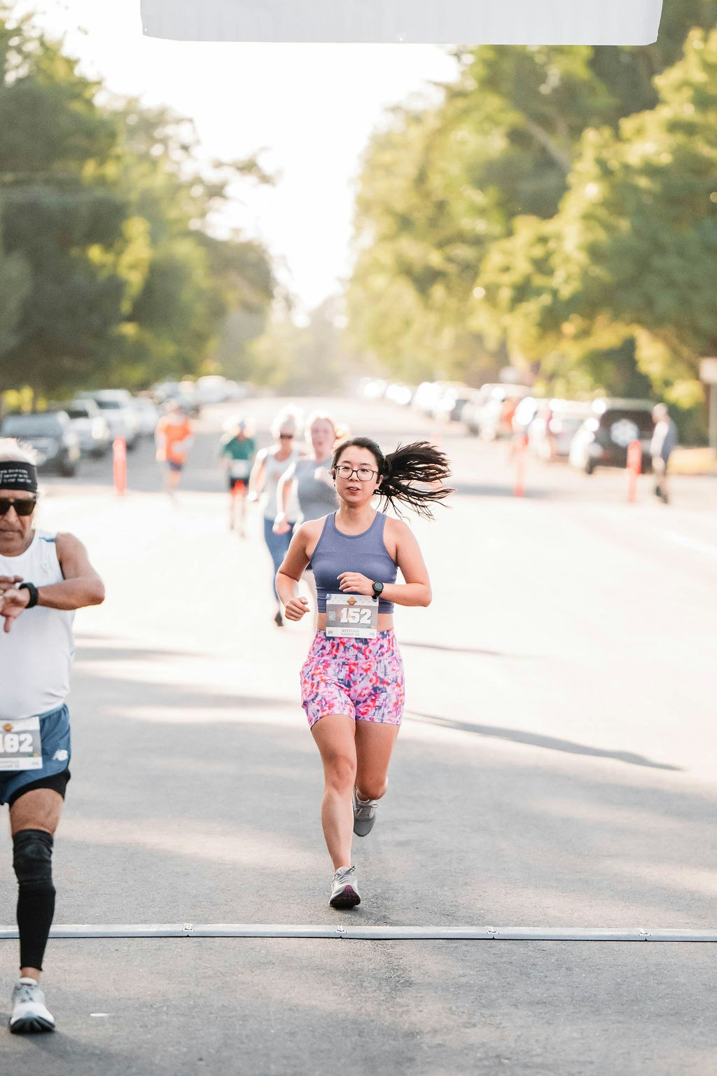 Runners nearing the finish line in an outdoor race; one woman leads.