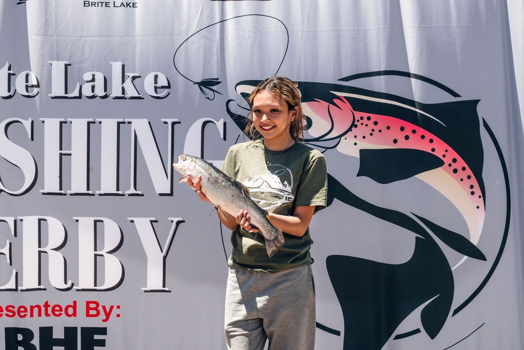 A person holding a fish in front of a banner for a Fishing Derby event.