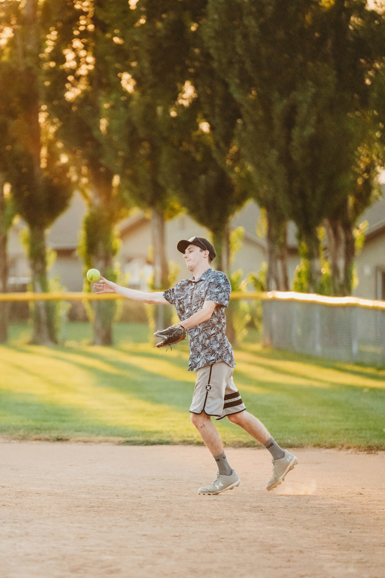 A person throwing a softball on a field at sunset.