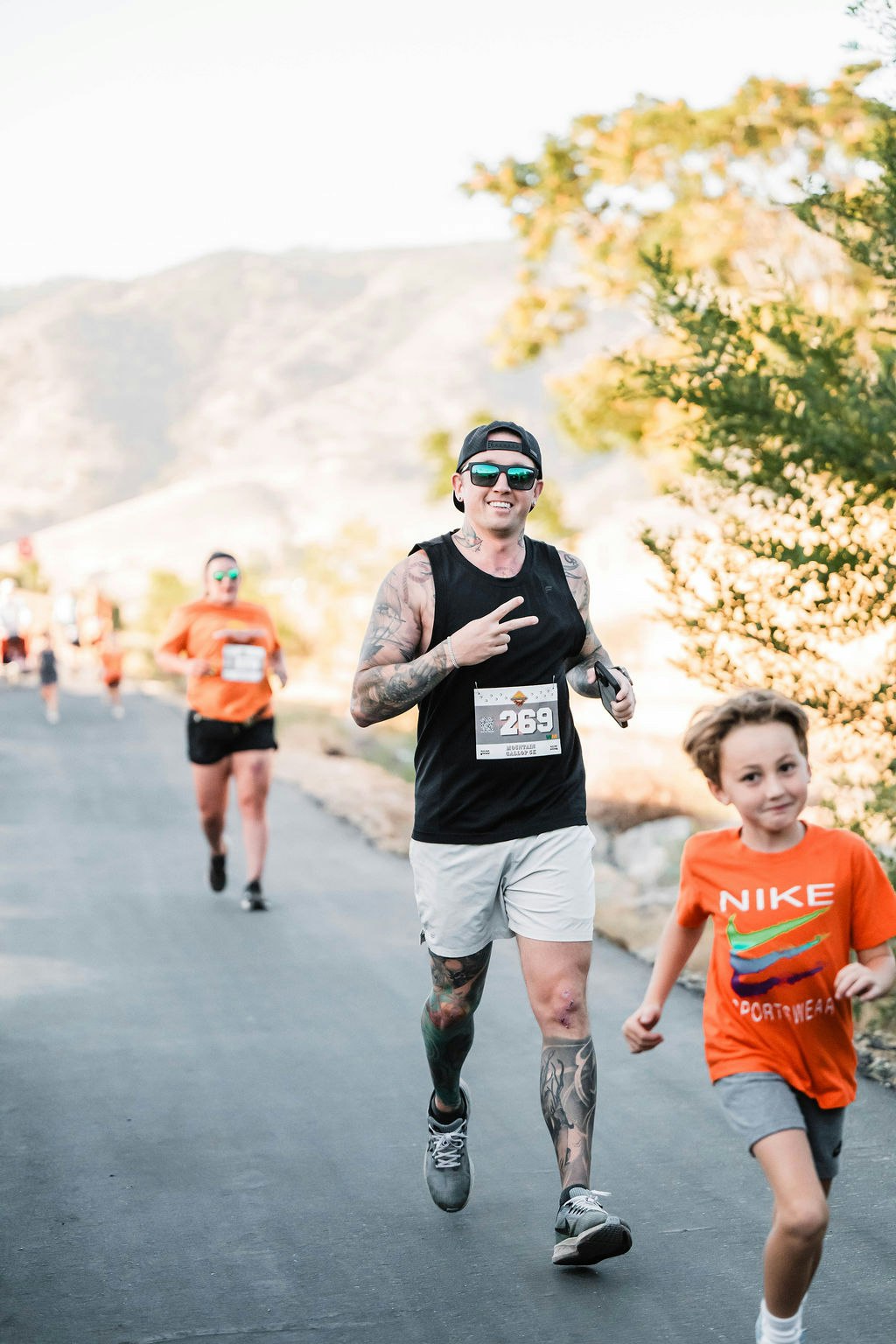People running on a road during a race; one is making a peace sign.