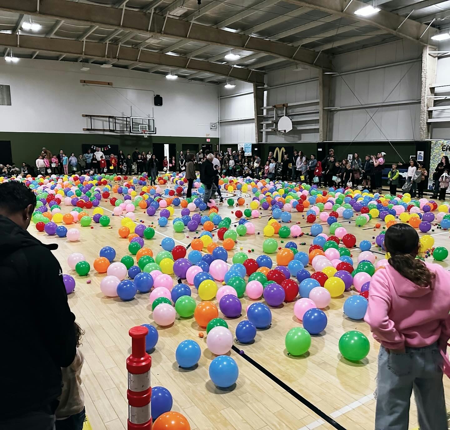 A gym filled with colorful balloons and people gathered around, some walking through the balloons.