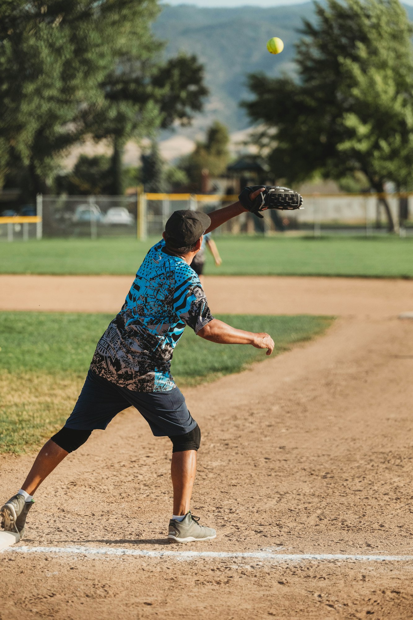 A person throwing a softball on a dirt field, glove extended, mid-action.