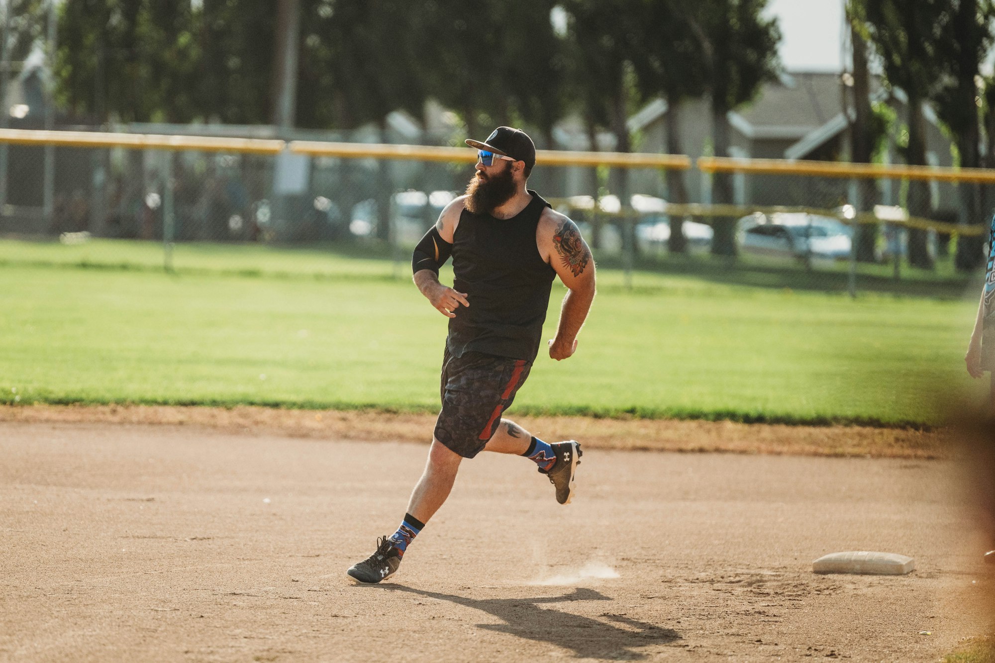 A bearded player in a cap and sunglasses running on a dusty baseball field.
