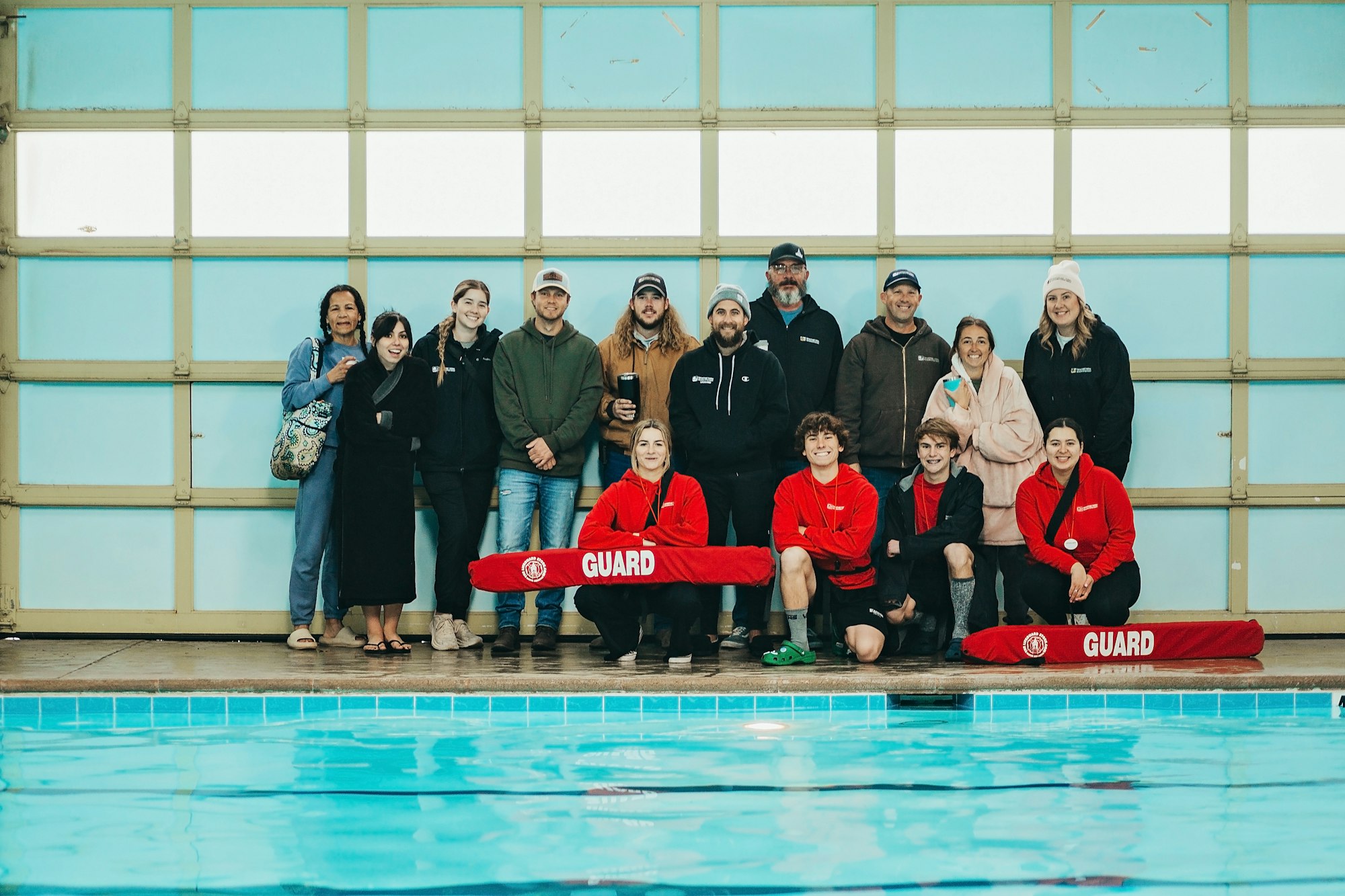 A group of people standing by an indoor pool, with some in lifeguard uniforms.