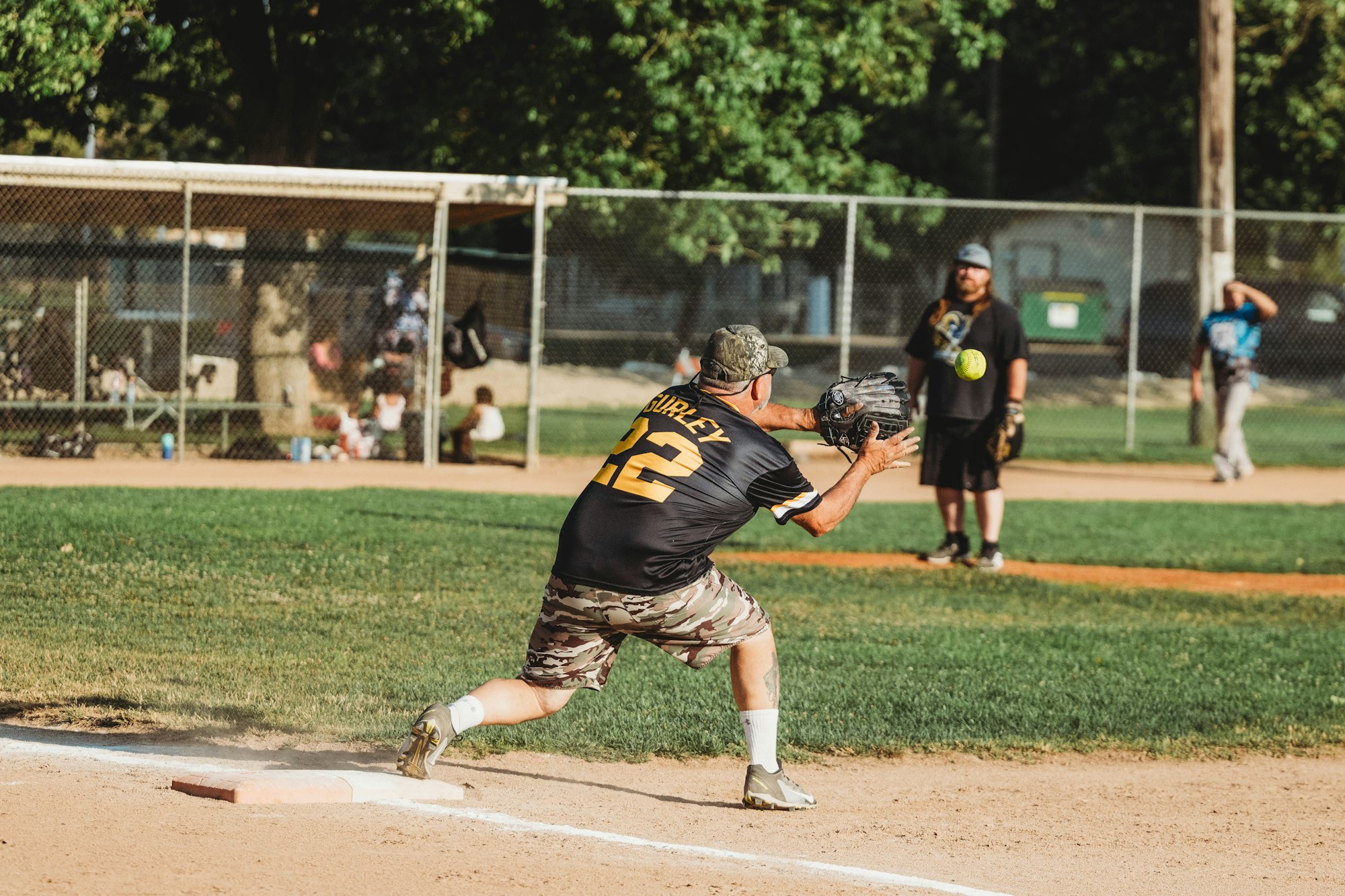 A softball player is about to catch a ball near first base.