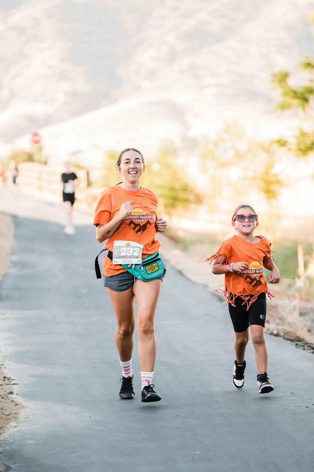 Two people running on a paved path, wearing matching orange shirts and smiling.