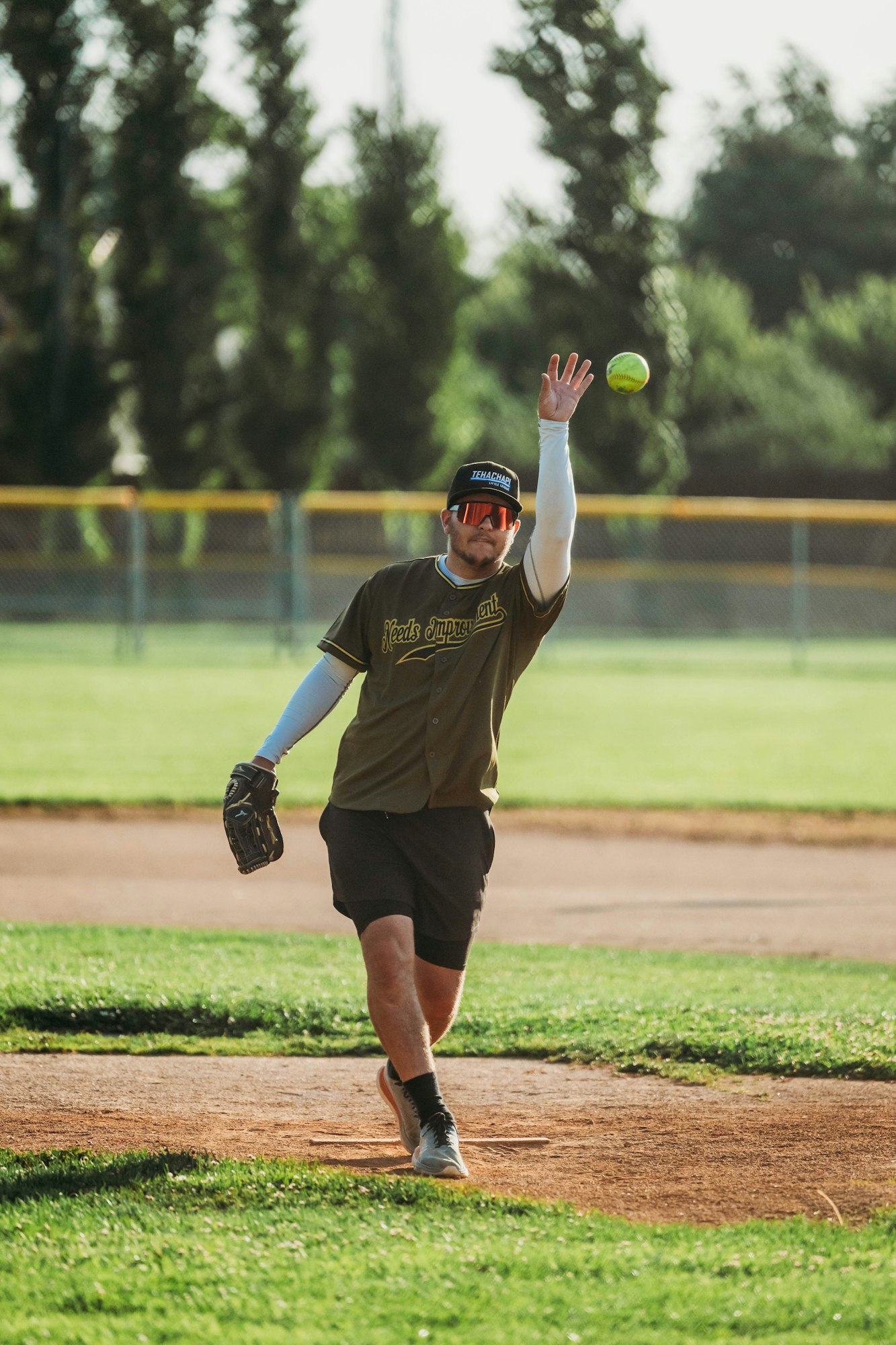 A person playing softball, pitching the ball on a sunny day at the park.