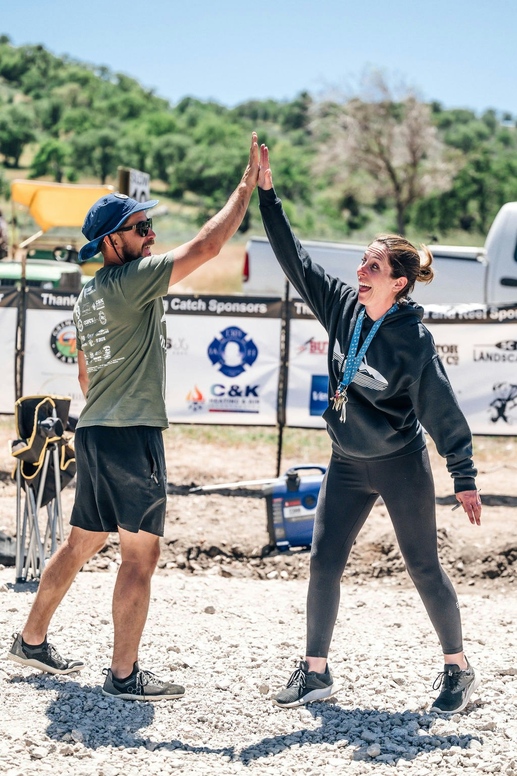 Two people high-fiving, smiling outdoors, with sponsorship banners in the background.