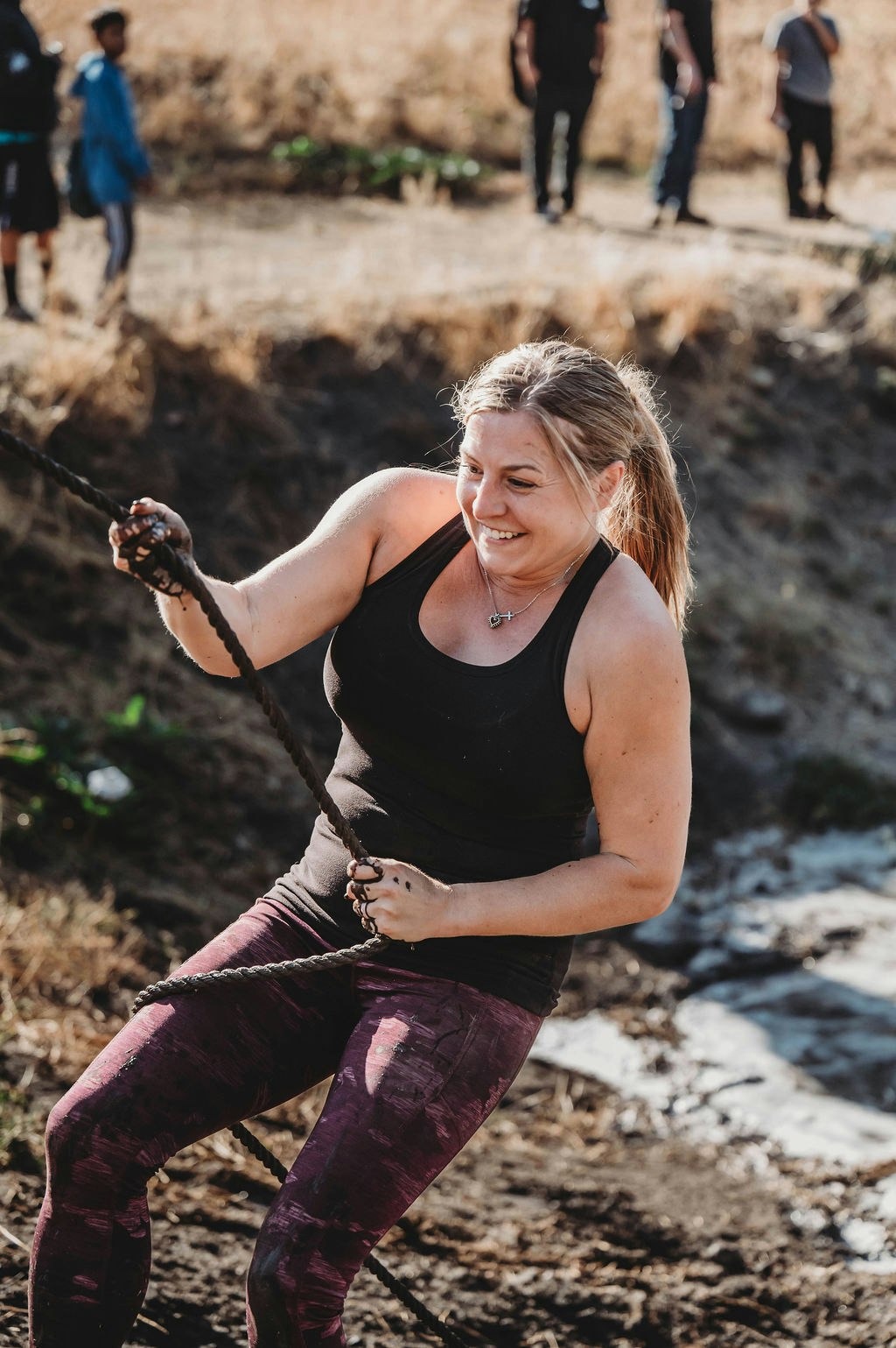 Person smiling while pulling a rope outdoors, with people watching in the background.