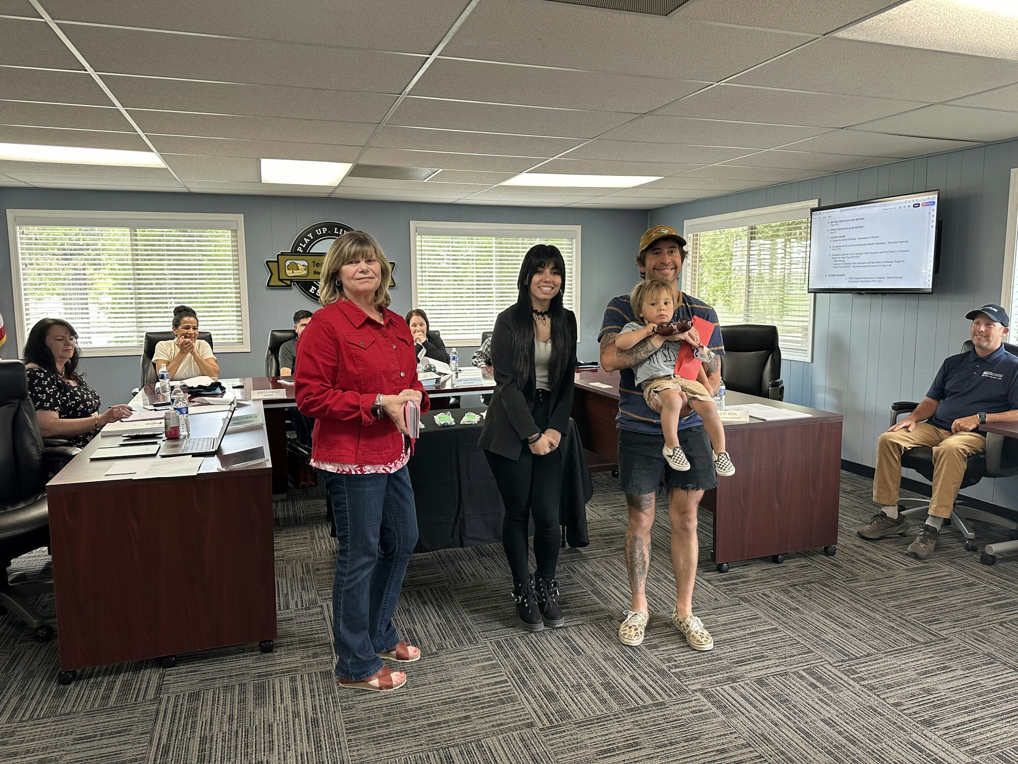 A meeting room with people, one holding a child and others sitting, possibly a formal gathering or presentation.