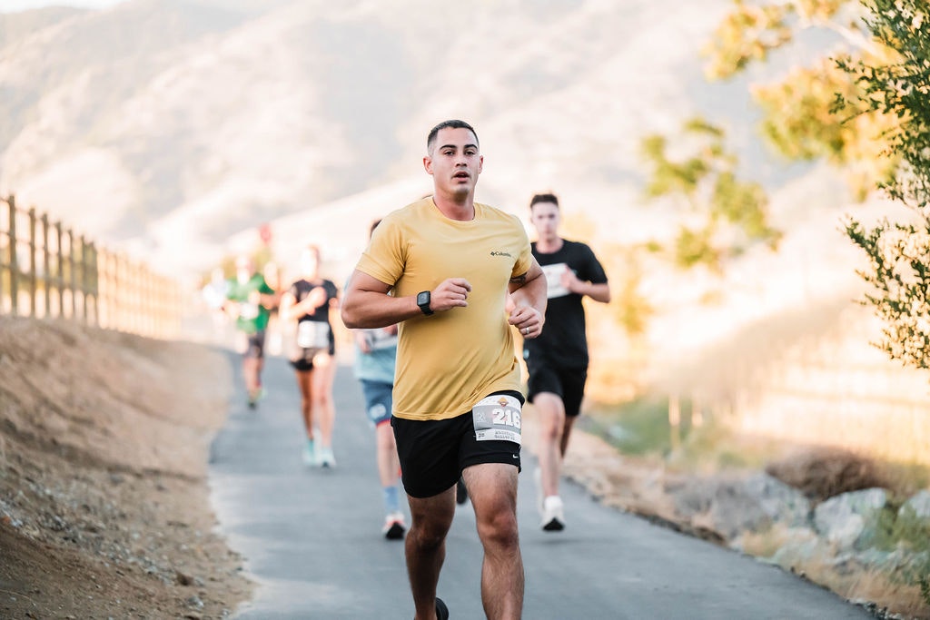 People running along a scenic outdoor path, one in focus wearing a yellow shirt.