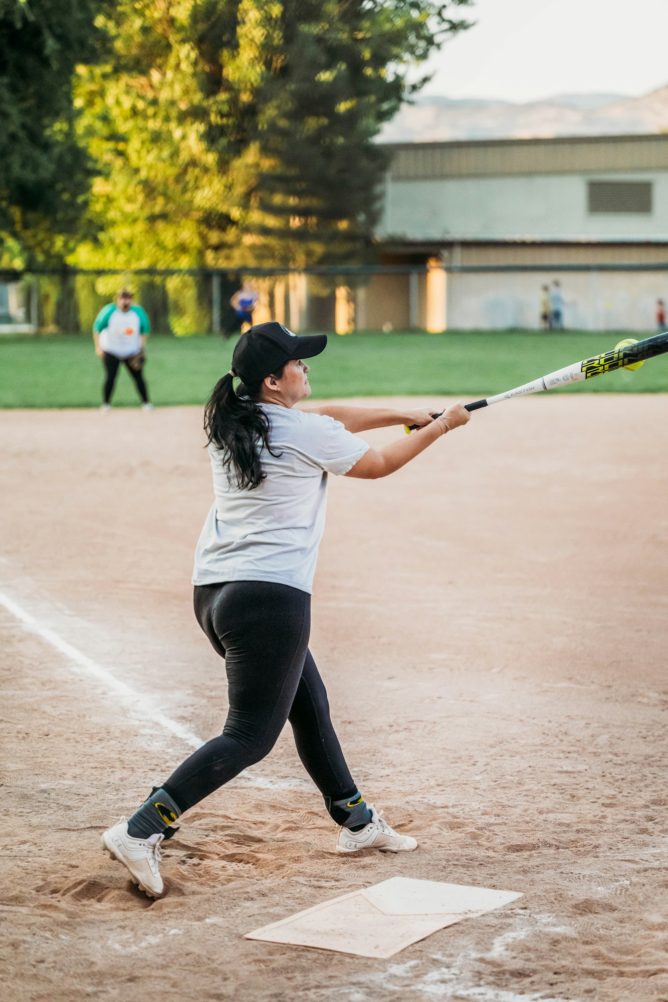 A woman is swinging a bat at a softball game, with players in the background.