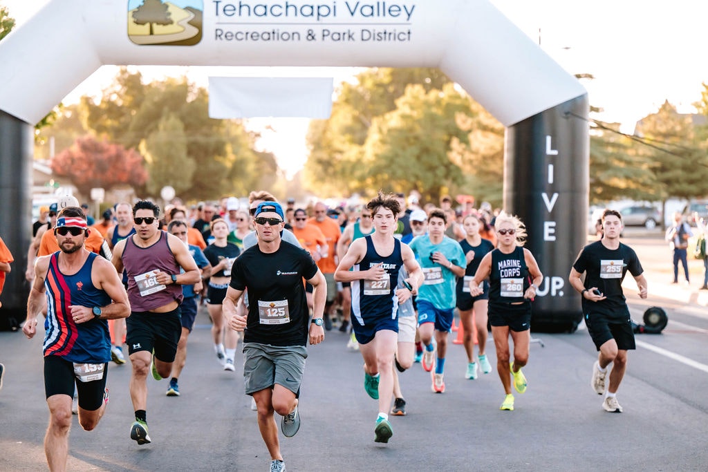 A group of runners participating in a race, passing under a "Tehachapi Valley Recreation & Park District" archway.