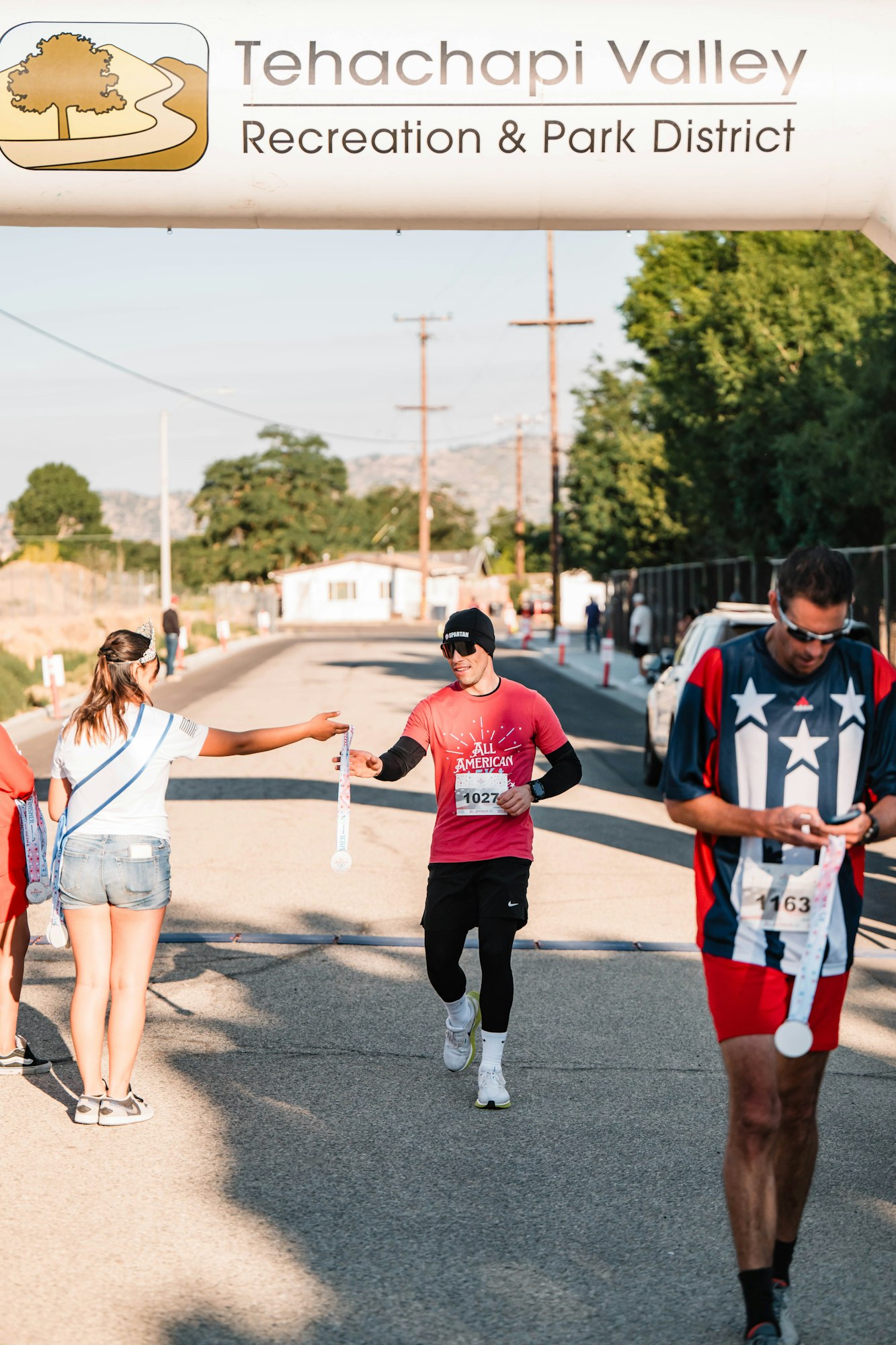 A runner receives a medal at a race finish line under a Tehachapi Valley Recreation & Park District banner.