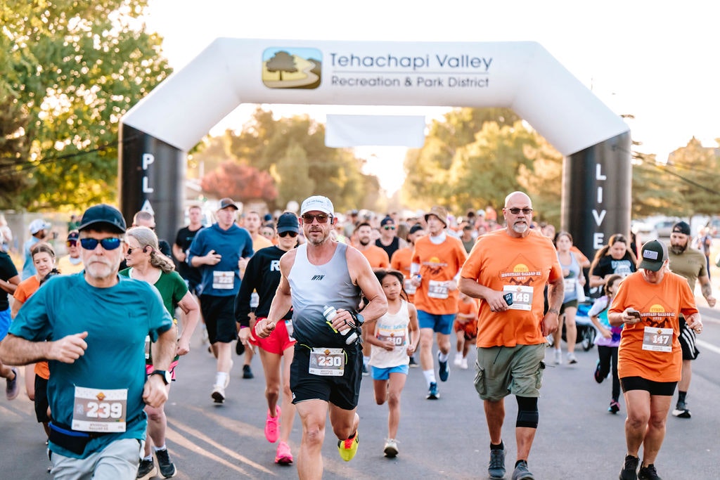 A group of runners participating in a race, with an inflatable arch labeled "Tehachapi Valley Recreation & Park District" in the background.