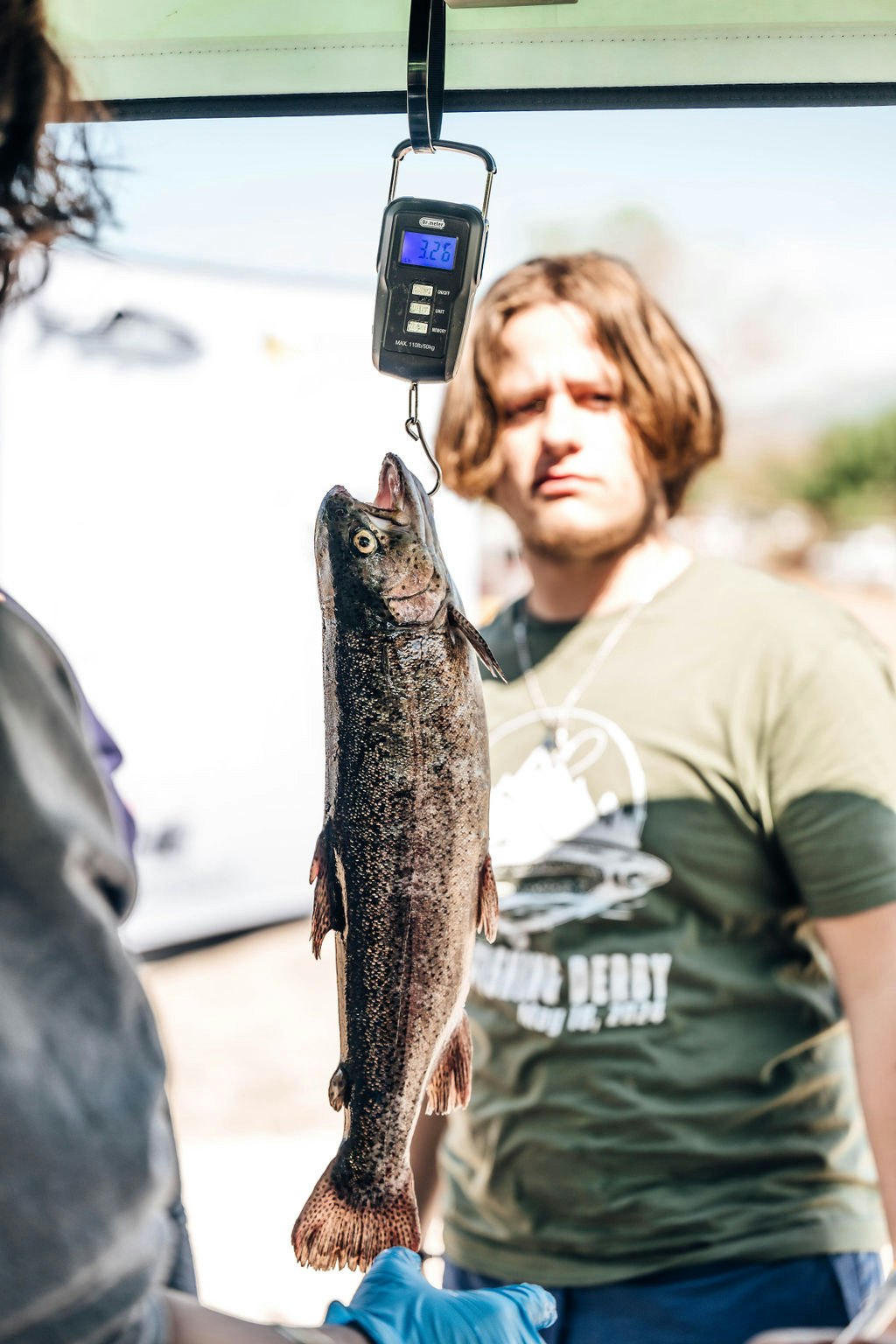 A person weighing a fish at 3.26 lbs on a digital scale.