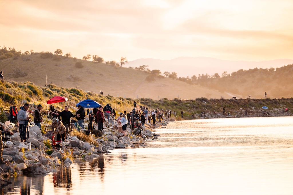 People fishing by a lake at sunset.