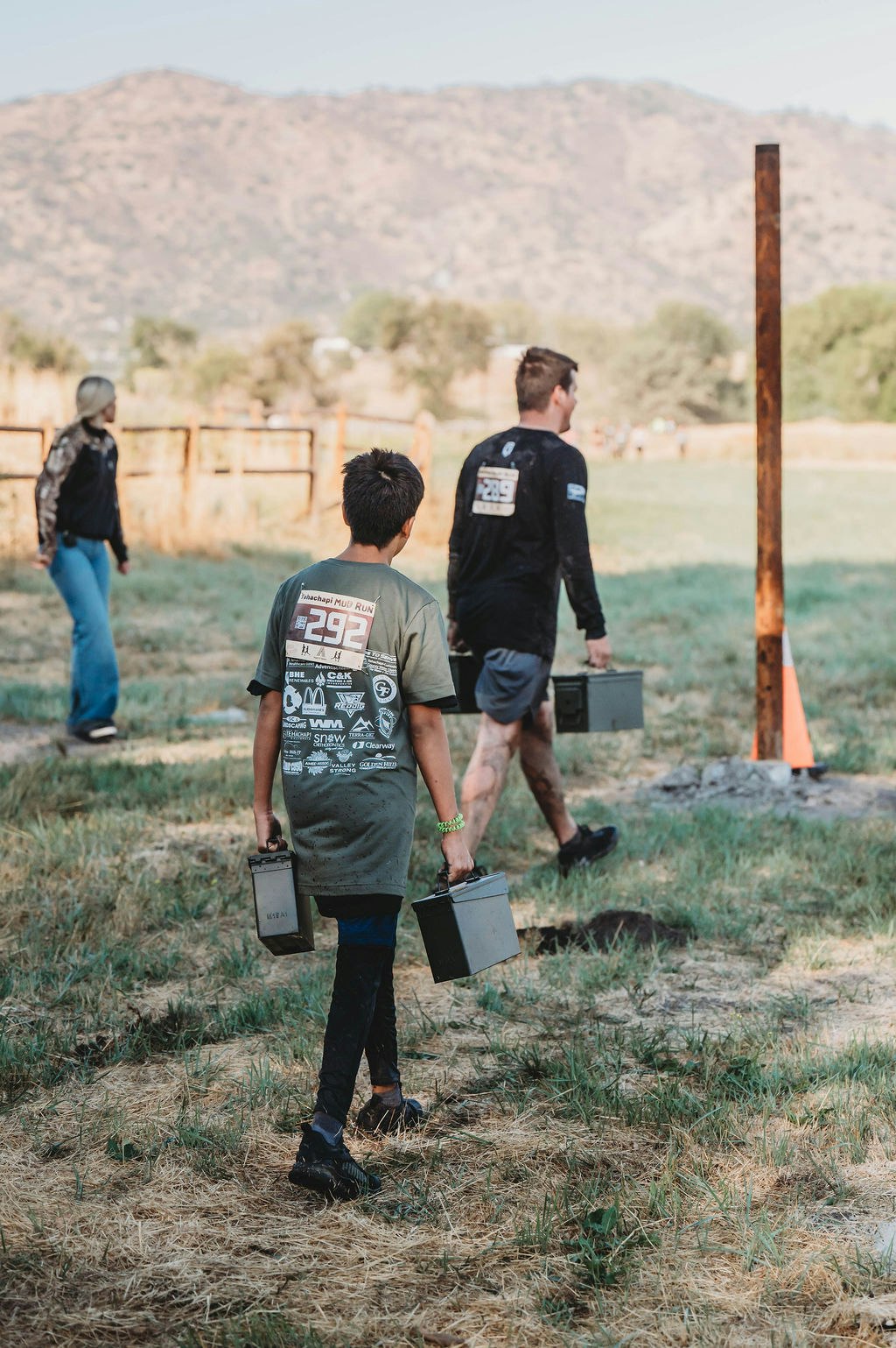 People are carrying containers on a grassy field, likely participating in an outdoor event or challenge.