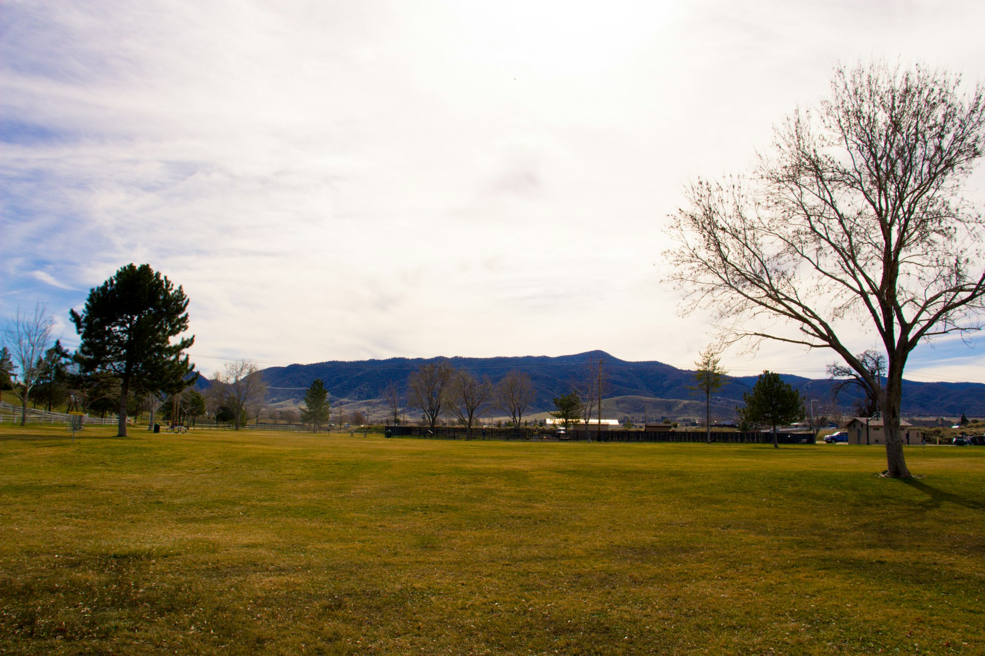 A park with trees, grass, mountains in the background, and a partially cloudy sky.