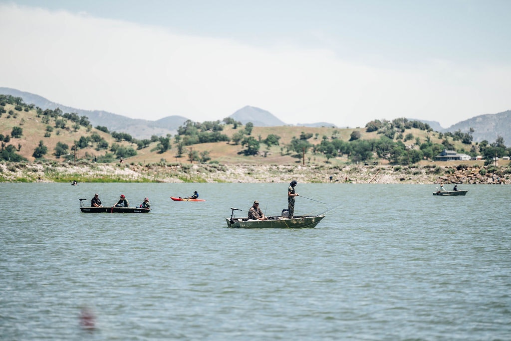 People in boats fishing on a lake with rolling hills in the background.