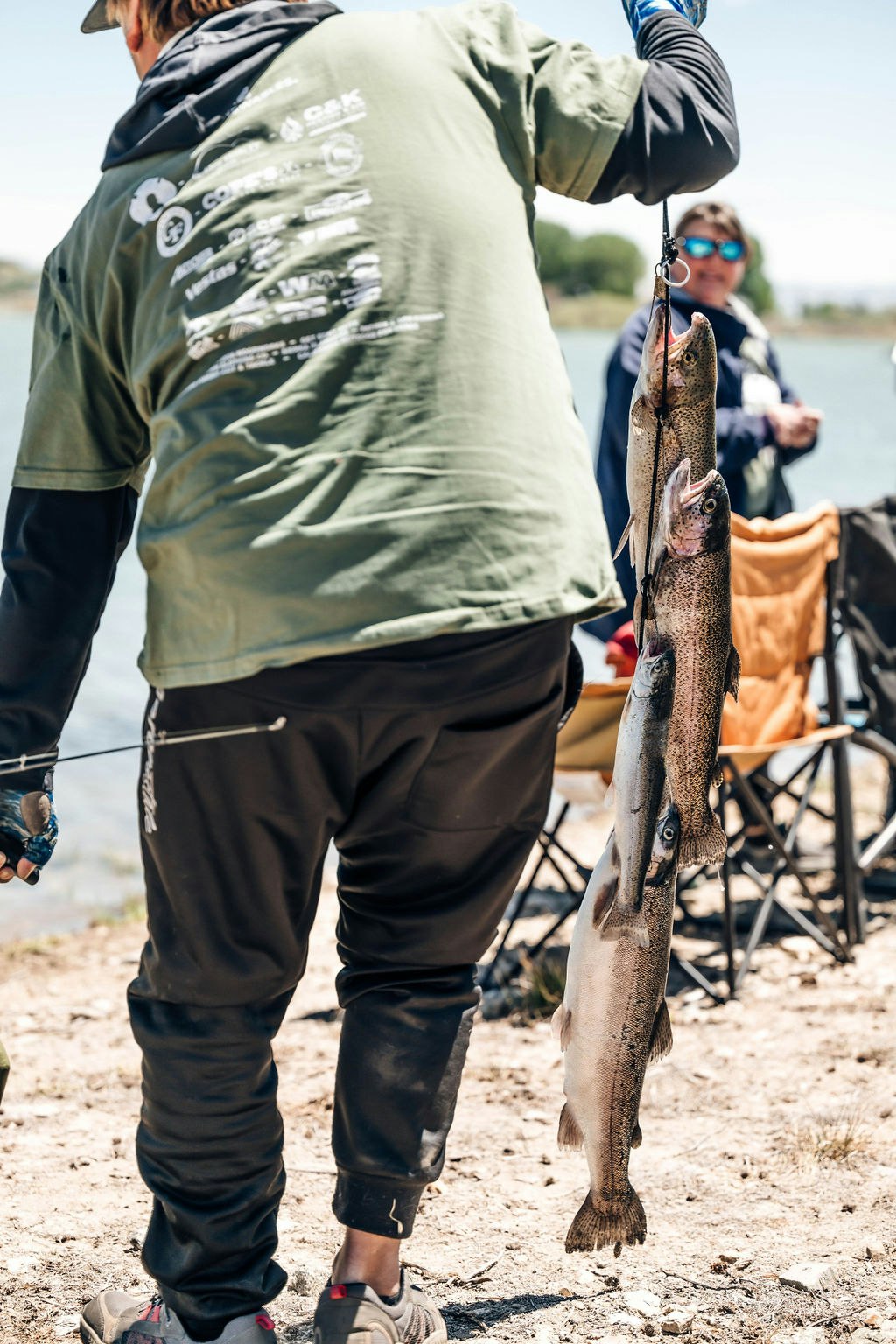 A person holding two fish on a scale, with another person observing in the background.
