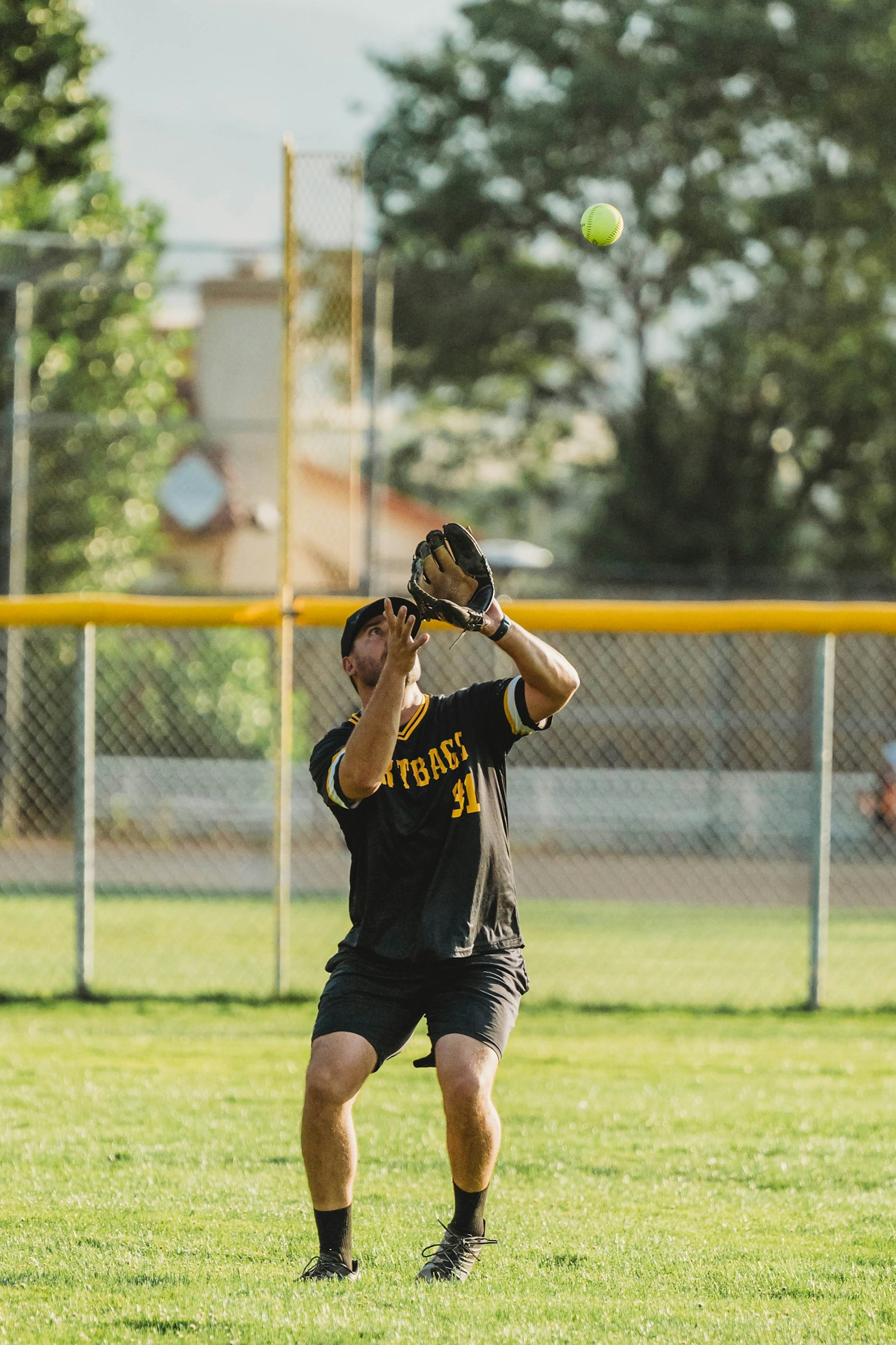 A player in a black outfit catching a softball on a sunny field.