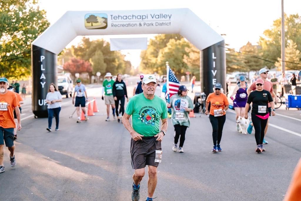 People participating in a race, passing under an inflatable arch with "Tehachapi Valley Recreation & Park District."