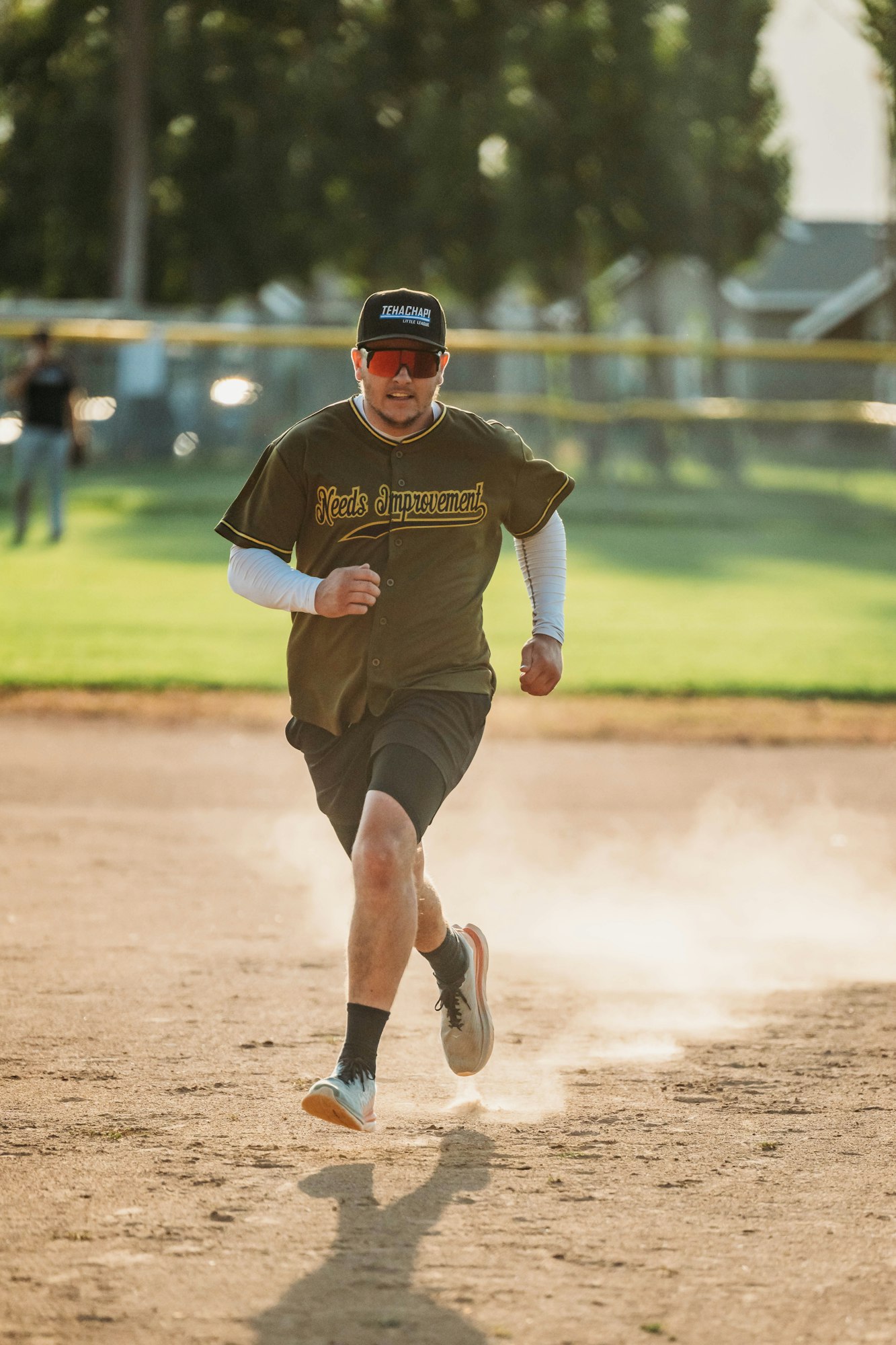 A person playing baseball, wearing a jersey that reads "Needs Improvement," running on a dusty field.