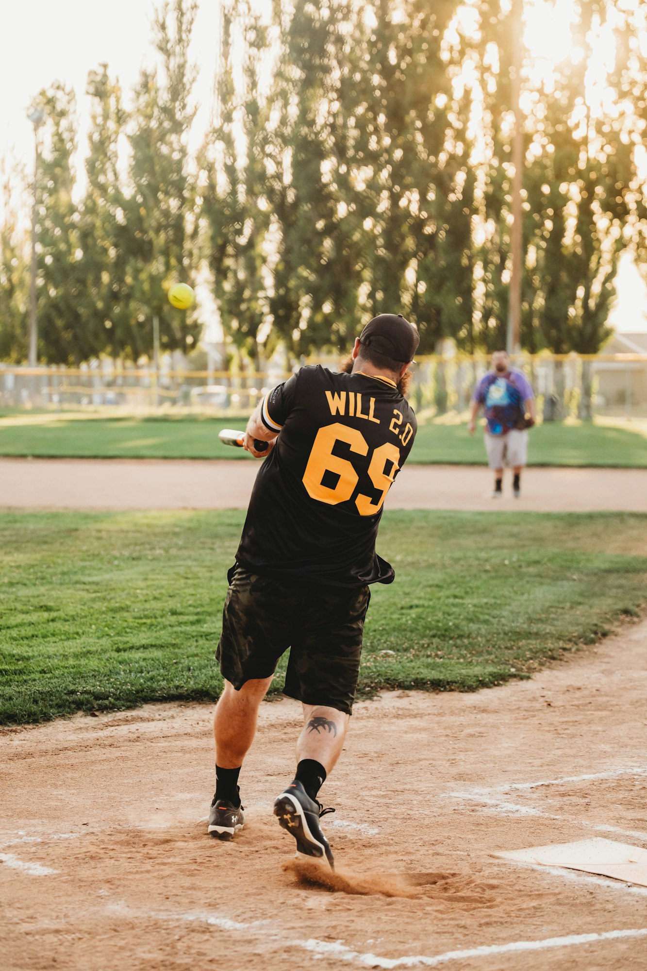 A person swinging a bat at a ball on a sunny baseball field.