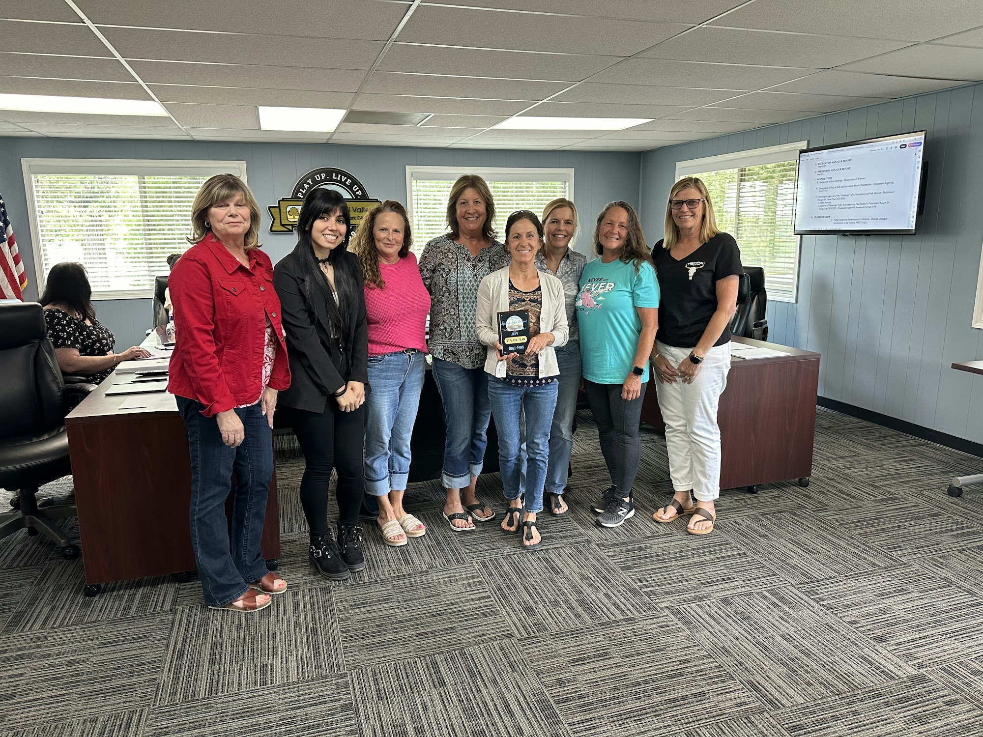 A group of people smiling in an office, with one person holding an award plaque.