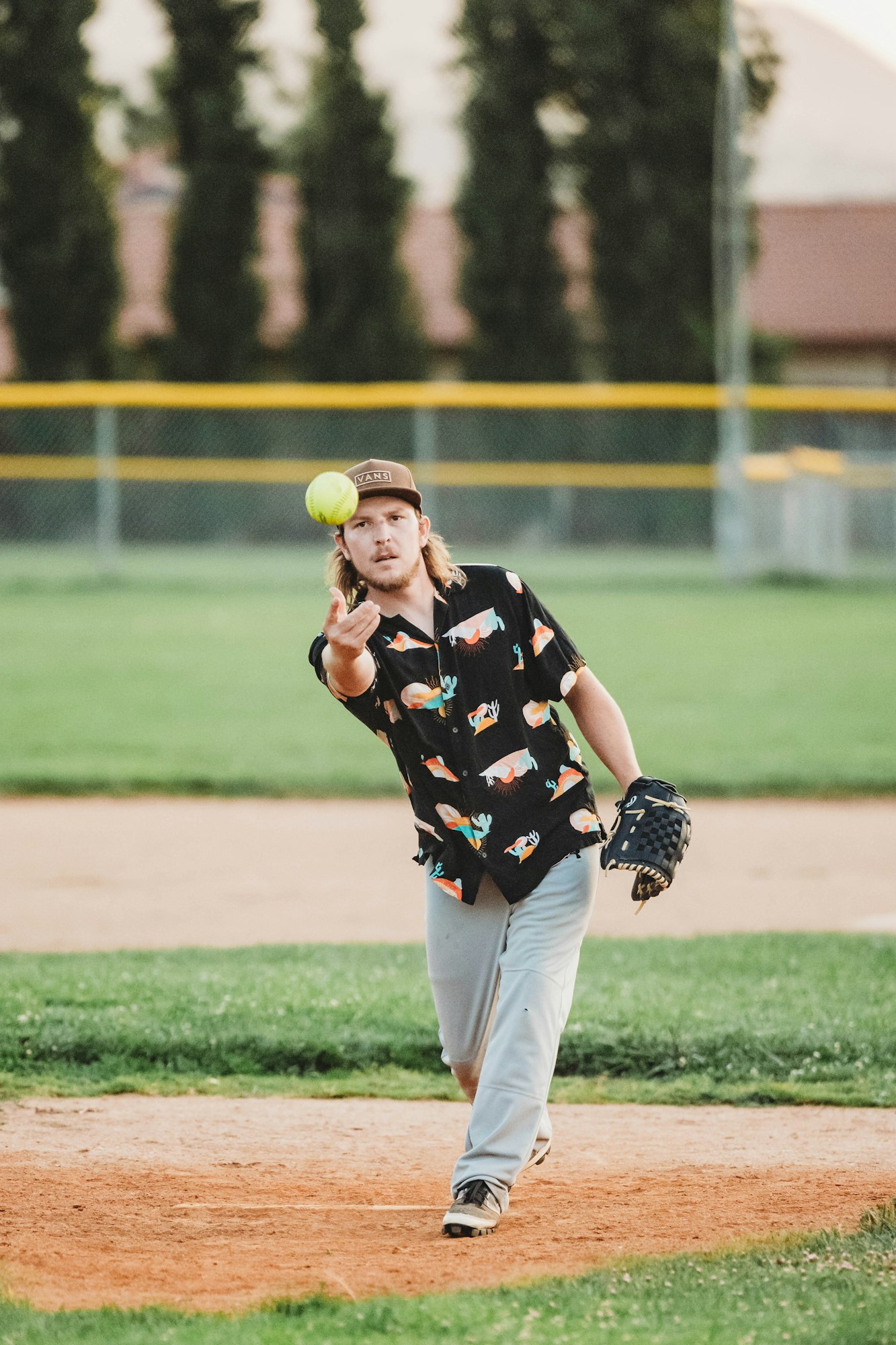A man pitches a softball, focusing on the incoming ball.